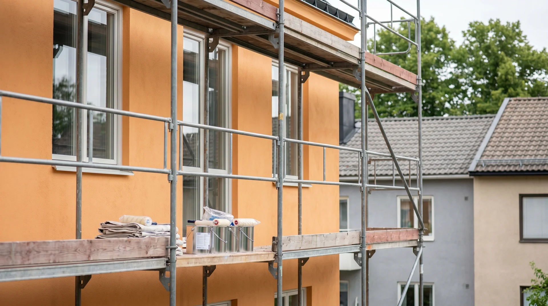Byggställning vid orange flervåningshus under renovering med verktyg och material.